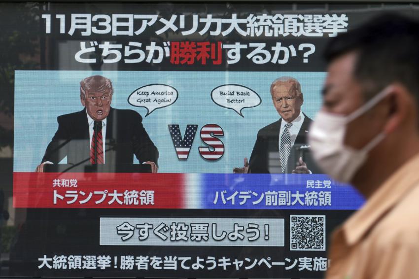 Um homem passa por uma tela mostrando ilustrações do presidente republicano Donald Trump, à esquerda, e do candidato democrata Joe Biden para a votação on-line para prever o vencedor na eleição presidencial americana de 3 de novembro, em Tóquio, na segunda-feira. Os japoneses no topo lêem: "Qual deles ganhará nas eleições presidenciais americanas de 3 de novembro".